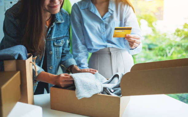 istock Two women holding and using credit card for online shopping while opening a postal parcel box of clothing 1266212739