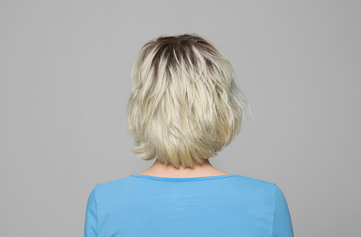 Rear view of woman in light blue top standing against grey background.