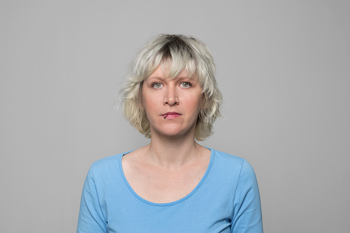 Portrait of serious woman in light blue top standing against grey background.