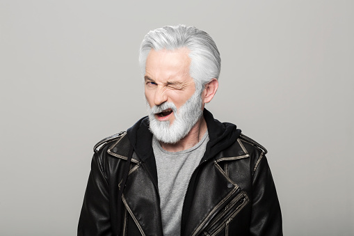 Portrait of senior man winking eyes standing against grey background.