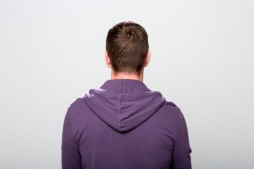 Rear view of mature man wearing purple hooded jacket standing against grey background.