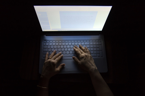 Female hands on a computer, working in the dark, at night causes much damage to the eyes
