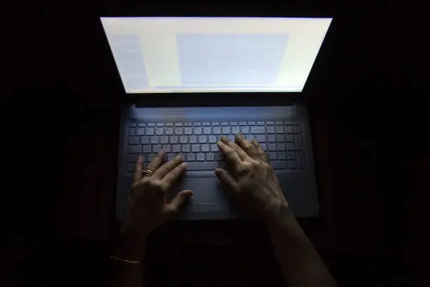 Photo of Female hands on a computer, working in the dark
