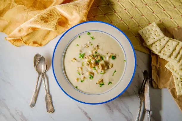 Fresh hot New England clam chowder soup with saltine crackers and parsley garnish