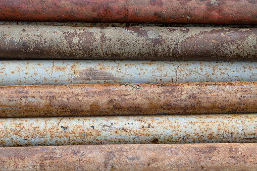 A background of steel technological pipes lying in parallel, covered with paint of different colors. There are rust and scratches on the metal surface. Texture