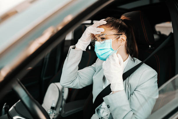 istock Young attractive brunette with face mask, with rubber gloves on holding her head because she is having headache while sitting in her car during corona virus outbreak. 1266223898