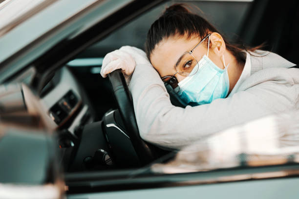 istock Bored attractive brunette with face mask with rubber gloves on leaning on steering wheel stuck in traffic jam during corona virus outbreak. 1266224928