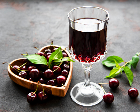 Cherry liqueur in a glass and fresh fruit on a black concrete background