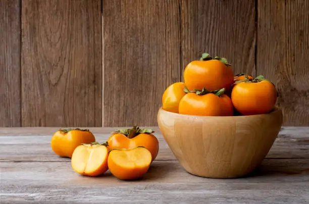 Fresh orange organic ripe Fuyu Persimmons or Persimon fruits in wooden bowl isolated on old wooden table background.Copy space for text and content.