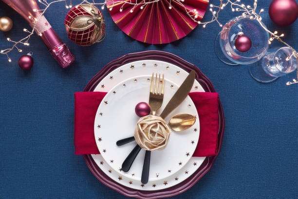 istock Christmas table setup with golden utensils, red deco. Flat lay on dark blue linen textile. 1266244152