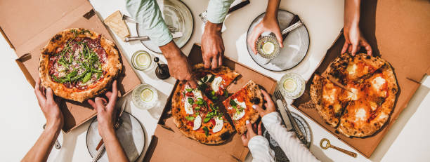 Pizzas in boxes, lemon drinks and peoples hands cutting pizzas