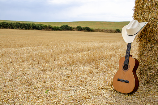 White cowboy hat and a Spanish guitar in a harvested wheat field.
