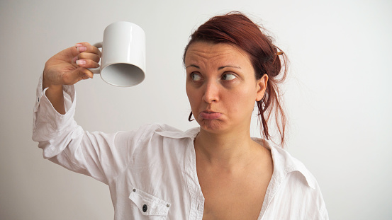 Sad woman holding empty cup upside down. When there is no morning coffee.