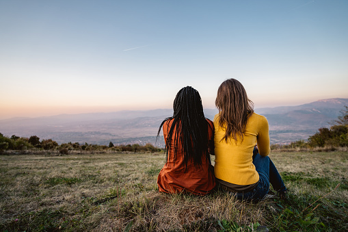 Multi-ethnic female friends sitting on meadow at sunset.