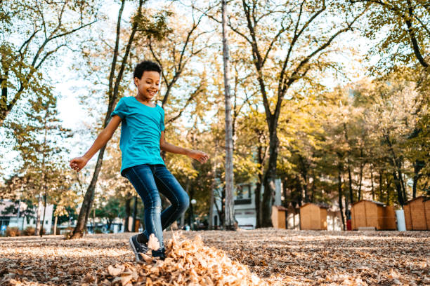Joyful mix race girl playing with autumn leaves in public park.