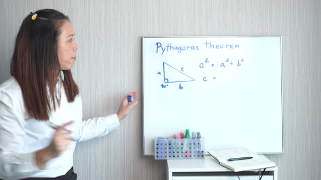 Teacher standing, teaching fundamentals of Pythagoras a whiteboard in a home for social distance and quarantine of COVID-19 pandemic for elementary school and homeschool. Asian black hair woman explaining additions about multiple numbers.