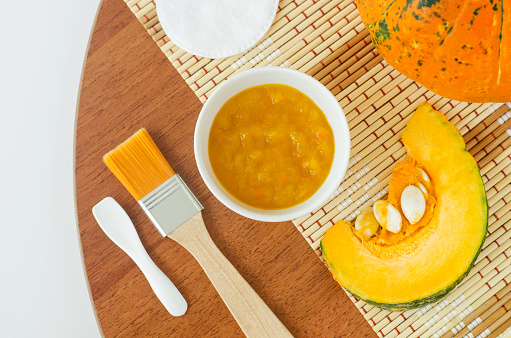 Fresh pumpkin puree in a small white bowl, cotton pad and cosmetic brush. Homemade face mask, natural beauty treatment and spa recipe. Top view, copy space.