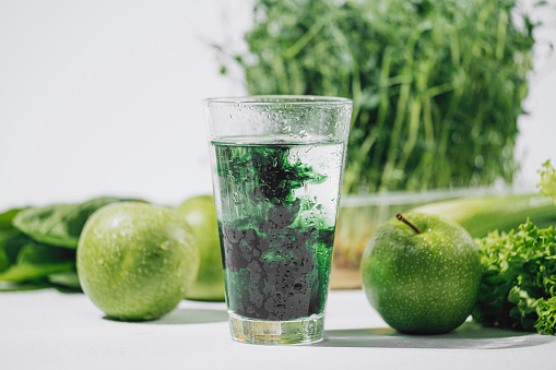 clorofila en un vaso de agua sobre un fondo blanco cerca son varias frutas y raíces de verduras frescas con lechuga y espinacas photo