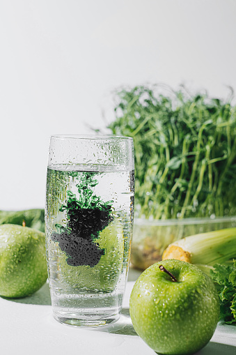 clorofila en un vaso de agua sobre un fondo blanco cerca son varias frutas y raíces de verduras frescas con lechuga y espinacas photo
