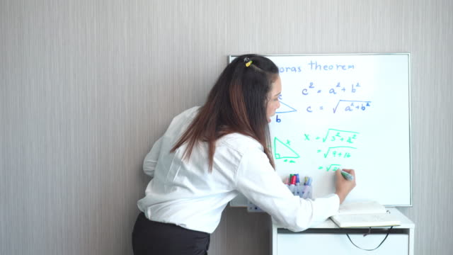 Teacher standing, teaching example of Pythagoras math a whiteboard in a home for social distance and quarantine of COVID-19 pandemic for elementary school and homeschool. Asian black hair woman explaining additions about multiple numbers.