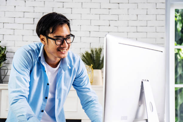 istock Young smiling happy asian man relaxing connected on internet with laptop computer working and video conference meeting at home.Young creative typing on keyboard.work from home 1266274144