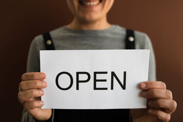 istock Woman with OPEN sign on brown background 1266283671