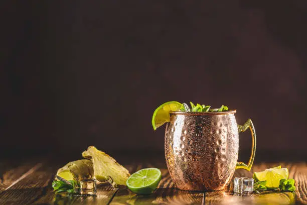Moscow mule alcoholic cocktail in copper mug with crushed ice, mint and lemon over minton dark wooden table with amazing backlight, copy space. Close up view, copy space