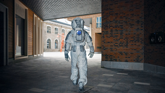 Low Angle Shot of a Confident Handsome Astronaut from the Back in a Neighbourhood with Modern Scandinavian Buildings. Man in Futuristic Suit with Technological Panel on His Hand.