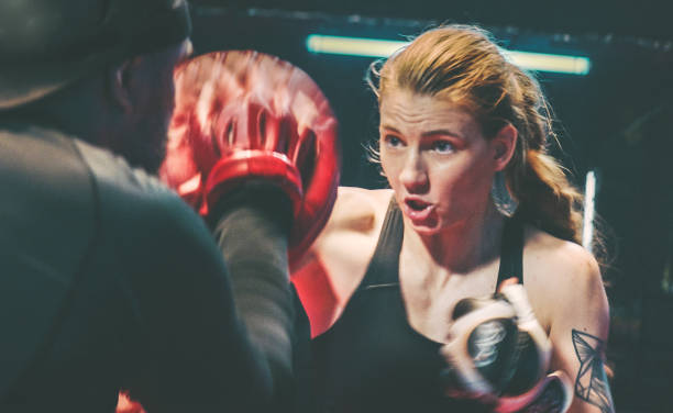 istock Female Boxer pad work session with trainer. Quick punches in octagon 1266292713
