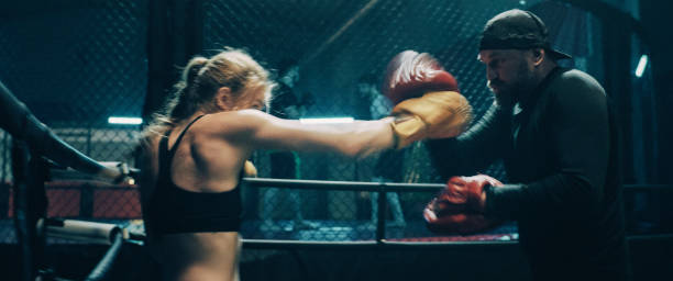istock Female Boxer pad work session with trainer. Quick punches in octagon 1266292972