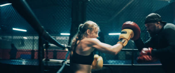 istock Female Boxer pad work session with trainer. Quick punches in octagon 1266292973