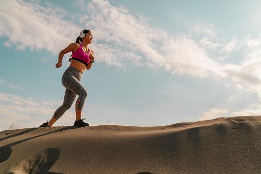 A female athlete is running on a hill on sand on a hot sunny day.
