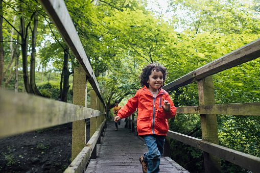 Mixed race young boy running through a rural area across a bridge while out on a walk outdoors.