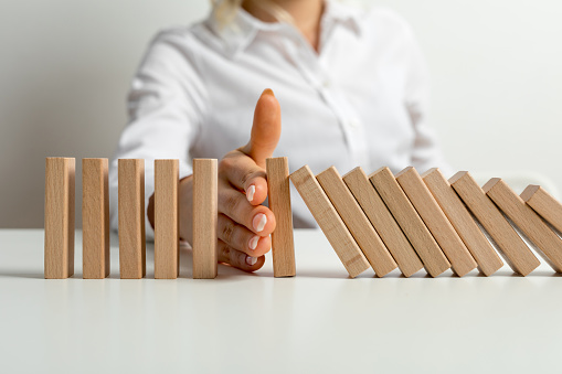 Businesswoman halting the domino effect inserting his hand between falling