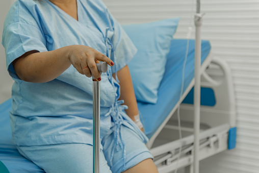 Overweight woman sitting on the bed with a cane in hospital.