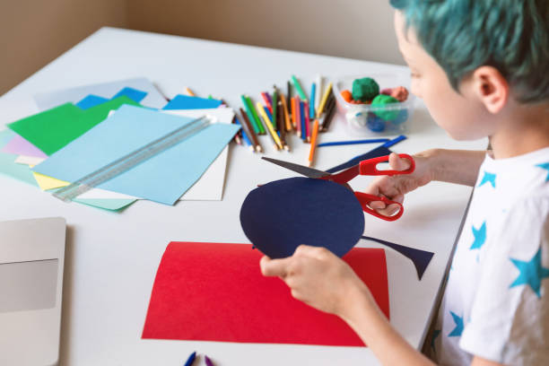 Boy cutting paper in arts and crafts class and making handmade gift.