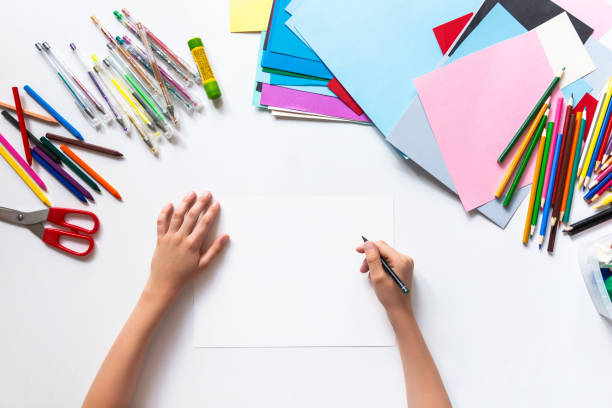 Unrecognizable child's hands drawing on blank paper. Top view