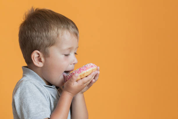 istock Happy boy eating donat on orange background 1266301859