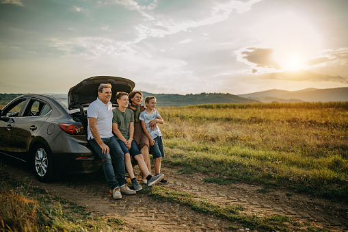 A shot of three mid-adult females standing beside the open boot of a car, getting ready for a walk in the countryside. They are packing their backpacks whilst talking and laughing together in a carpark in The Lake District, Northern England.
