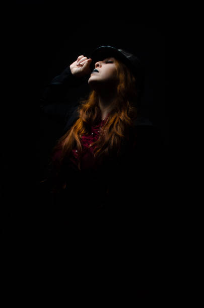 istock Portrait of a beautiful redhead with hat made in studio, low key image, with black background. 1266307261