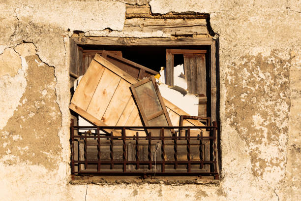 Front view of a boarded up aged old stained grungy window with small bars in a weatehred and ruined wall.