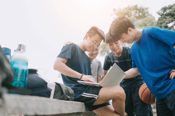 バスケットボールコートの横にあるアジアの中国の10代の少年のグループで、試合後に議論と集まりを行う - teenager child student social gathering ストックフォトと画像