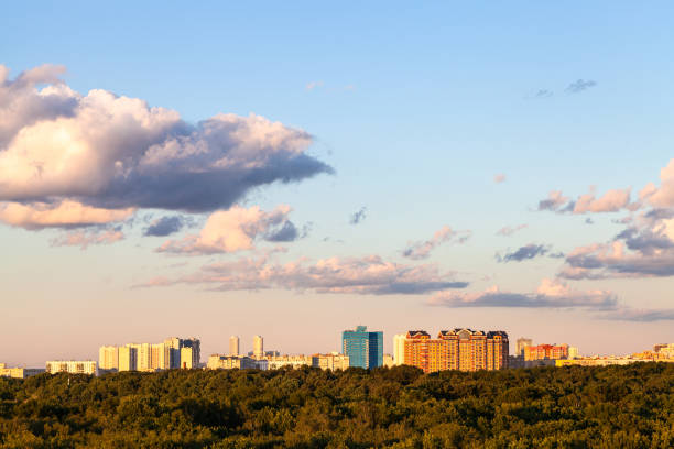 sunset blue and pink sky with and gray clouds over city and green forest in sunny summer evening