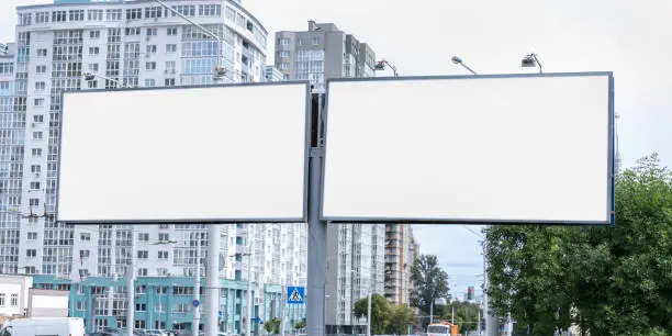 Photo of two big white empty billboards on pole at city street commercial advertising concept