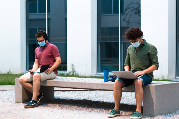 Two college students learning while keeping social distance on campus. Technology and Coronavirus concept. stock photo