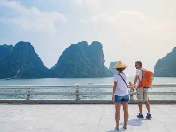 Couple walking hand in hand on promenade at Halong City, Vietnam, view of Ha Long Bay rock pinnacles in the sea. Man and Woman having fun traveling together on vacation to famous landmark.