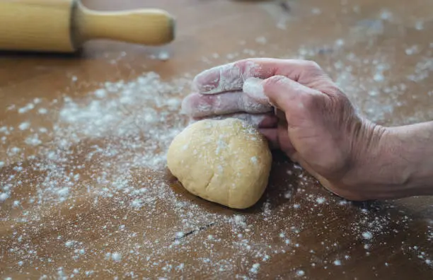 Man's hands kneading bread on a wooden table with flour sprinkled on a wooden roller in the background. Bakery concept.