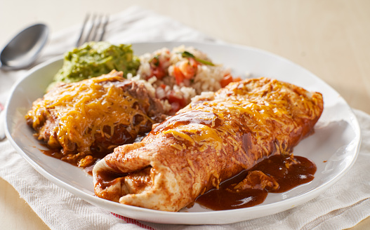 mexican wet burrtio platter with red enchilada sauce, refried beans, rice and guacamole close up