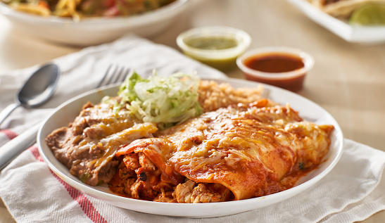 mexican enchilada platter with red sauce, refried beans and rice close up