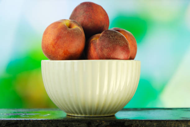 Peaches in bowl on natural green background.